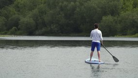 caucasian man on supboard. a man in blue shorts stands and rows with an oar on a board. a man spends time on the water. slow motion video. High quality Full HD video recording