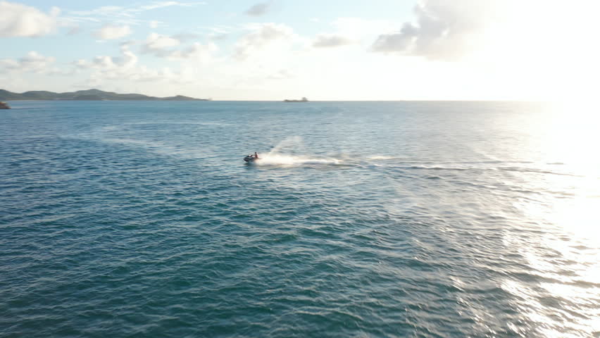 Aerial tracking circular view male on jet-ski ride maneuver have fun at full speed with sunset over horizon. Antigua and Barbuda fun water sports activities and holiday destination