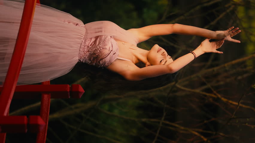 Beautiful Young Woman in Pink Dress, arms Raised to the Sky, Sensual Pose, Standing on Red Wooden Bridge, Forest, Slow Motion, Vertical