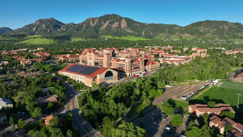 Wide shot of University of Colorado Boulder campus. Aerial establishing shot of college campus with buildings with red roofs and mountains in background.
