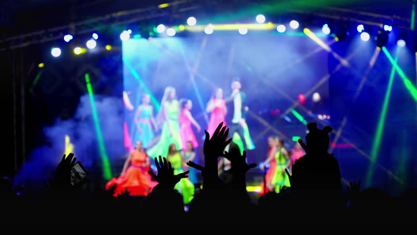 Happy people watching amazing musical concert. Bright colorful stage lighting. Nightlife and entertainment concept. People with raised arms on music event with lights. 4K, UHD Royalty-Free Stock Footage #1106863495