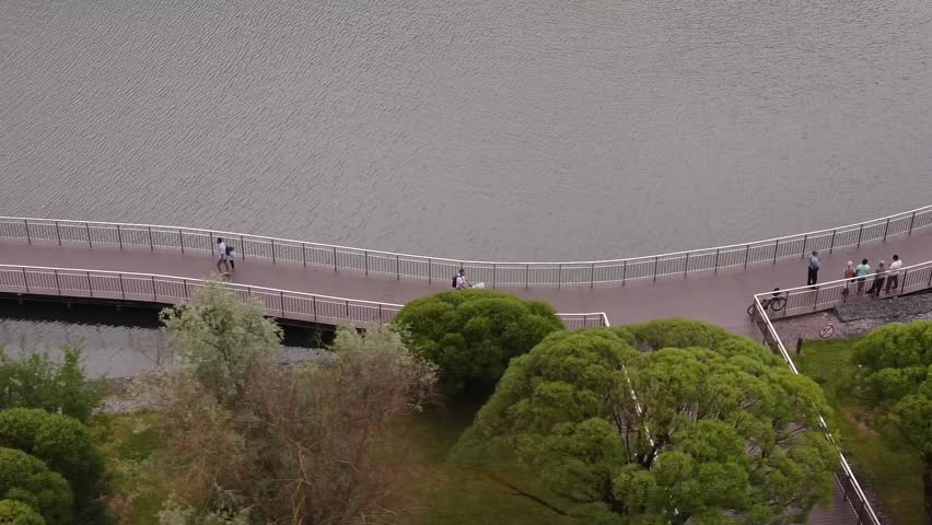 Aerial view of people walking with their families on a pedestrian bridge on the shore of a lake in a modern park in summer