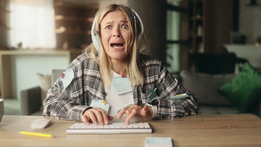 Camera view of nervous stressed blond mature woman freelancer with stickers typing quickly on computer and looking at papers asking to hurry up scream and warning about deadline at home workplace