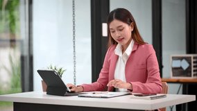  Beautiful Asian woman using laptop and tablet while sitting at her working place. Concentrated at work.
