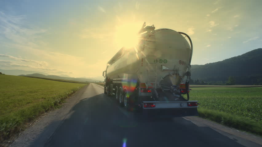 Sunlit oil tanker driving on road at sunset back view tracking shot. Fuel truck riding on countryside highway, transporting liquid on summer Royalty-Free Stock Footage #1106882505
