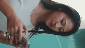 Vertical video: Beautiful brunette girl in headphones dressed in casual clothes, goes and uses mobile phone on blue wall background
