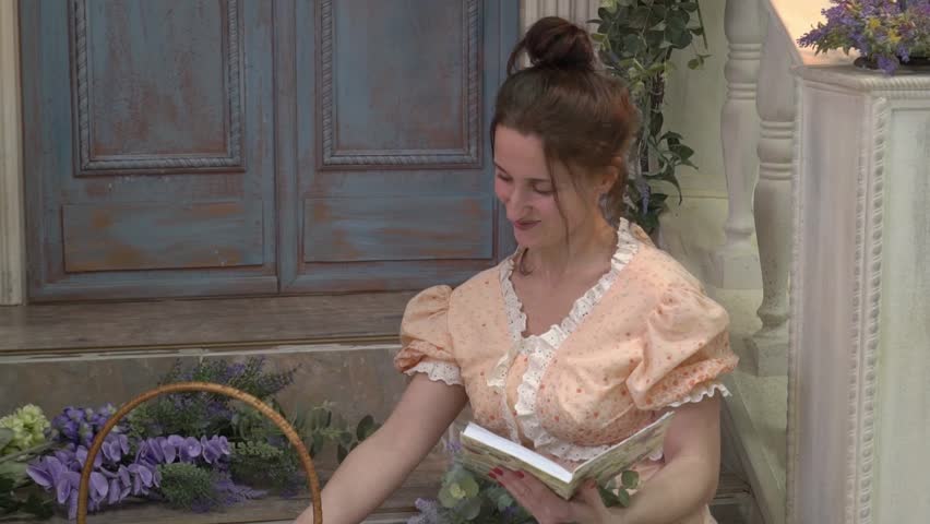 Woman in dress sits reading book with a duckling in a basket. 