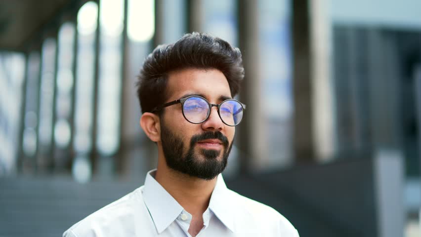 Close up portrait of a young businessman in a shirt and glasses smiling and looking at the camera. Handsome male posing standing on the street in front of an office building. Head shot of the manager Royalty-Free Stock Footage #1106887773