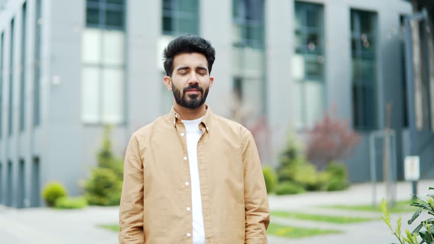 Portrait of a young bearded businessman smiling and looking at the camera. Handsome male in caged clothes posing with crossed arms on the street in front of an office building. Head shot of employee | Shutterstock HD Video #1106887789