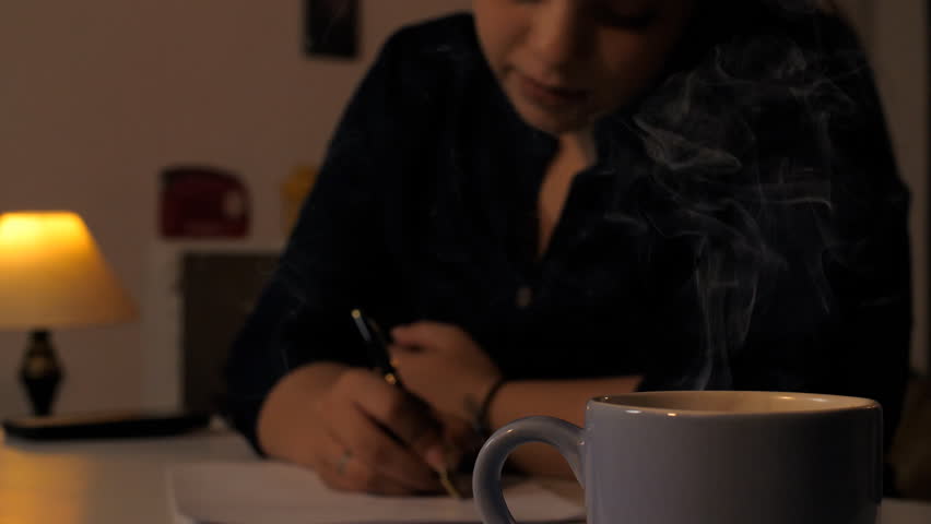 Indian woman preparing for her exams at home - Mid night studies, education, concentration. Asian Indian woman making her notes in a lamp light in a dark room with a hot coffee on the table - Stude...