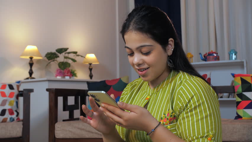 A beautiful Indian woman playing mobile games and is excited, victory gesture, mobile gaming. A pretty teenage girl addicted to online games, over dependence on mobile phones, winning gesture, succ...