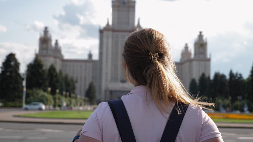 A view from the back of a female student with a backpack on her back, she stands and looks at the large building of the state University. The first day of college. Moscow State University. Royalty-Free Stock Footage #1106890791