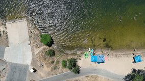 sideways overhead aerial footage along the sandy beach at Silverwood Lake with rippling water and lush green trees, grass and plants in Hesperia California USA