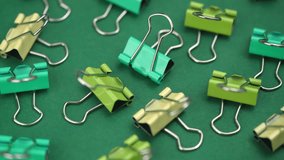 bright multicolored metal paper clips rotate on a green background. a collection of stationery for office documents and administration. closeup.