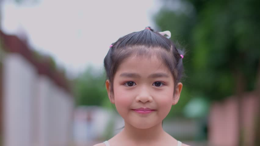 Portrait of an attractive little Asian girl smiling and look camera and wave her hand, happy smiling child looking at camera - close-up, outdoors. Joyful nature childhood leisure concept. Royalty-Free Stock Footage #1106898257