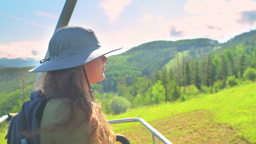 Young woman on ski lift gondola chair, sitting in summer at Beaver Creek resort of Vail Resorts, Colorado on sunny day in hiking hat Royalty-Free Stock Footage #1106899915