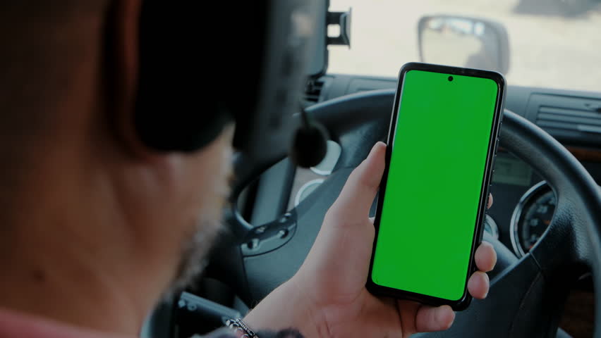 The driver in the truck holds a phone with a green screen in his hands. rear view close up  Royalty-Free Stock Footage #1106903485