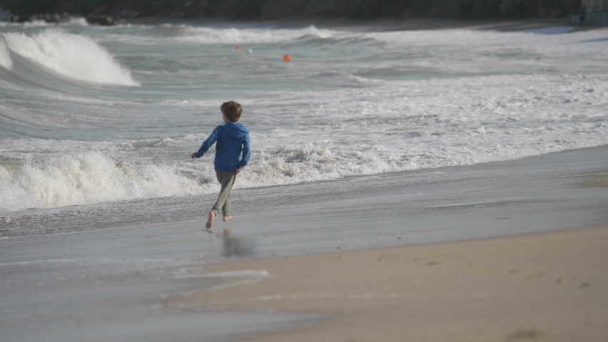 Little kid running on beach and playing avoid waves at seaside during summer vacation