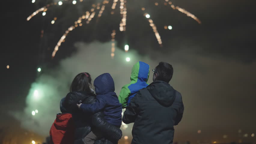 Parents holding little kids watch the New Year's Eve fireworks Royalty-Free Stock Footage #1106908071