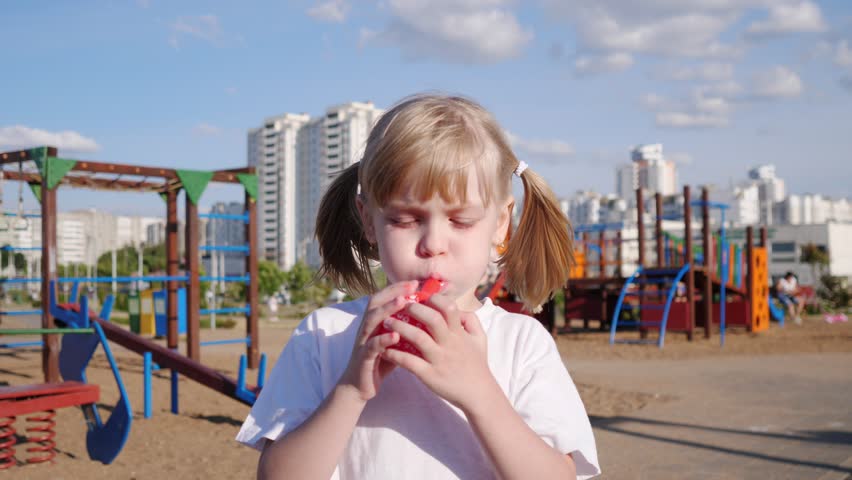 Little cheerful girl portrait inflates a red balloon on the playground in summer 4k slow motion
