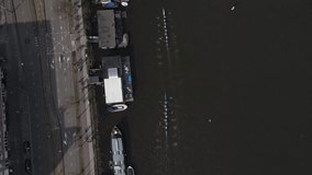 A beautiful top down drone shot following two rowing 8+ boats while they perform in a regatta. Many cyclist follow them along the river.