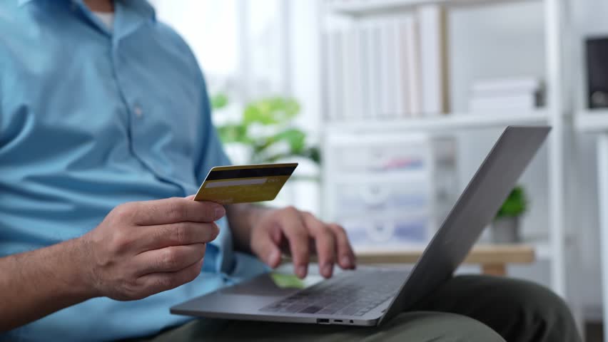Happy hispanic young man consumer holding credit card and laptop buying online at home. male shopper customer shopping on ecommerce website market place making digital payment using bonus money. Royalty-Free Stock Footage #1106918943