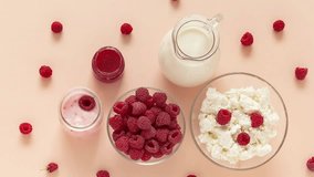 Video of summer organic dairy products and fresh raspberries for breakfast. Jug of milk, bowl of cottage cheese, Greek yogurt with raspberries on pastel pink background. Copy space, flat lay, close-up