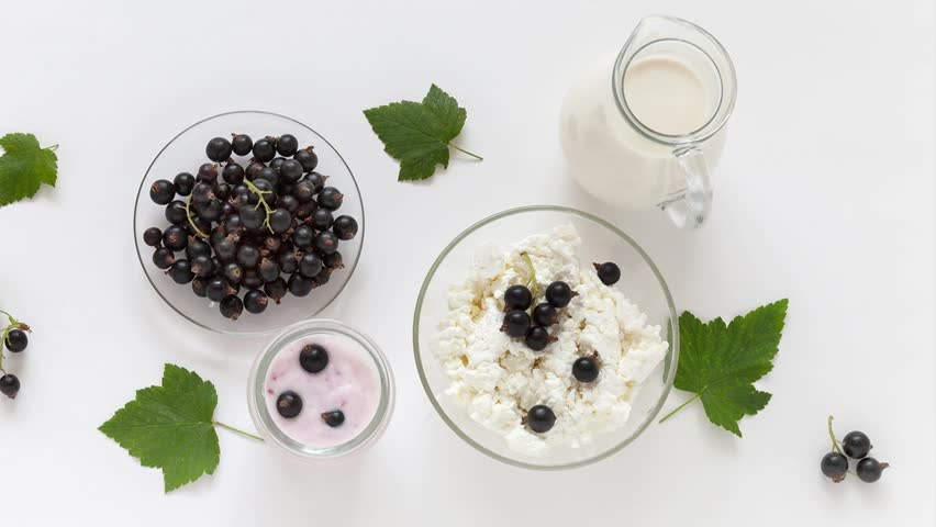 Video of ripe garden blackcurrants and summer organic dairy products for breakfast. Jug of milk, bowl of cottage cheese and Greek yogurt with berries on white background. Flat lay, top view, close-up Royalty-Free Stock Footage #1106920411
