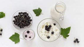 Video of ripe garden blackcurrants and summer organic dairy products for breakfast. Jug of milk, bowl of cottage cheese and Greek yogurt with berries on white background. Flat lay, top view, close-up