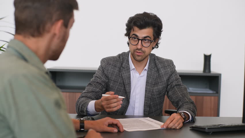 Portrait of male real estate broker wearing business suit present and advise young man client on decision to sign insurance contracts. Happy male customer signing purchase agreement and shaking hands. Royalty-Free Stock Footage #1106920437
