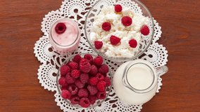 Video of rustic still life with organic dairy products, fresh raspberries for breakfast. Jug of milk, bowl of cottage cheese and Greek yogurt with raspberries on handmade lace napkin on wooden table