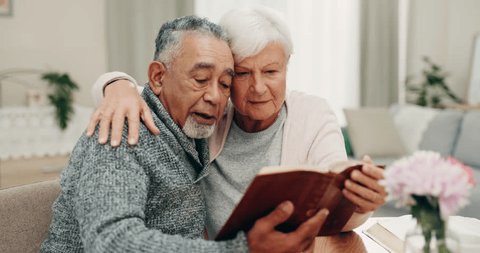 Bible, God and a senior couple reading a book in their home together for religion, faith or belief. Love, Jesus or Christ with a spiritual man and woman in worship or prayer during retirement Stockvideó