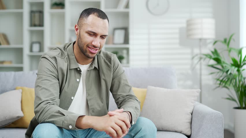 Sad handsome male suffering from toothache while sitting at home in living room. Young adult guy suffer from terrible painful tooth ache, sensitive teeth cavities Indoor in a modern interior Royalty-Free Stock Footage #1106930561