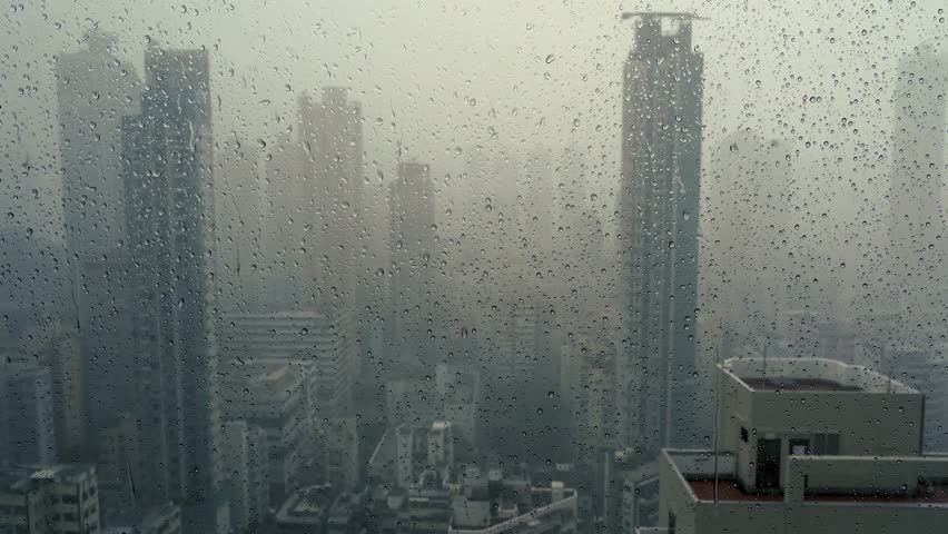 Rain falling on window in skyscraper apartment. Dark and stormy rainy day in big city life. View of dreary Hong Kong cityscape whilst rain drops fall on the window. Abstract somber moody background. Royalty-Free Stock Footage #1106931575