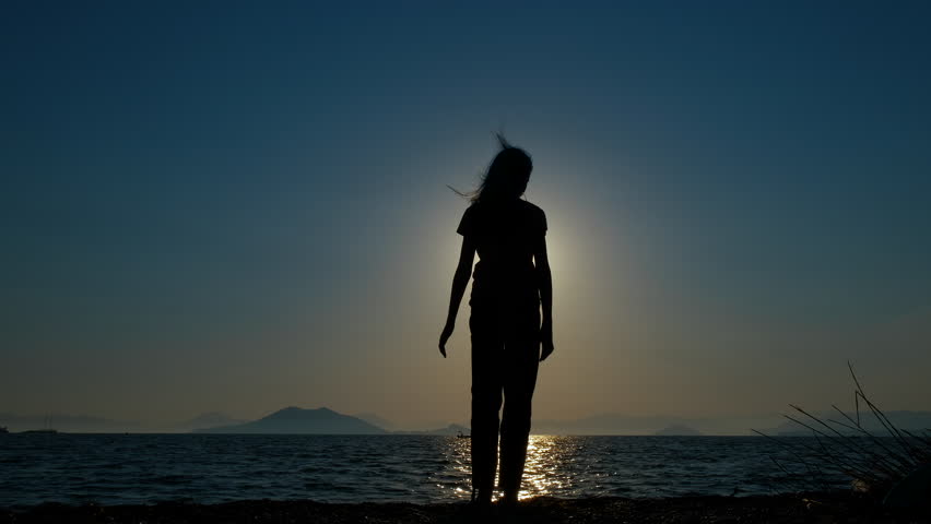 Girl silhouette doing shadow waves. A girl silhouette dancing with hands on the empty shore against sunset sky in summer. A concept of active and playful children summer.