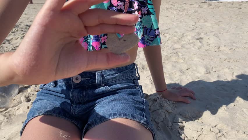 She rubs a small heart out of the sand with her hands