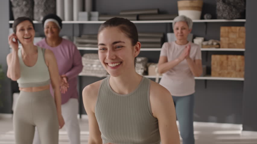 Young female fitness trainer smiling and showing aerobics exercise to group of senior people in sportswear while having workout together in studio Royalty-Free Stock Footage #1106934839