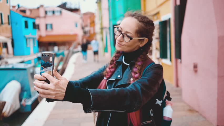 Traveler blogger taking selfie photo near colorful houses on Burano island in Venetian lagoon. Travel and vacation in Italy concept. Lifestyle travel moments in the beautiful italian city. | Shutterstock HD Video #1106936263