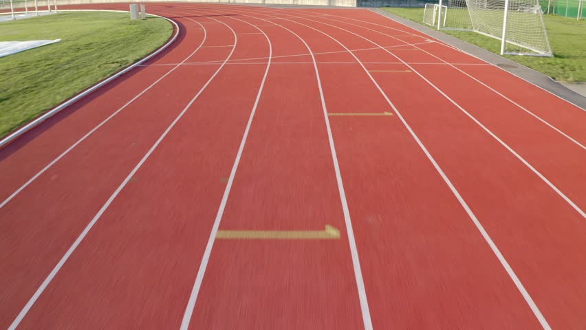 Tour over the red oval athletic track with eight lanes on an outdoor stadium, tracking shot. Royalty-Free Stock Footage #1106936489