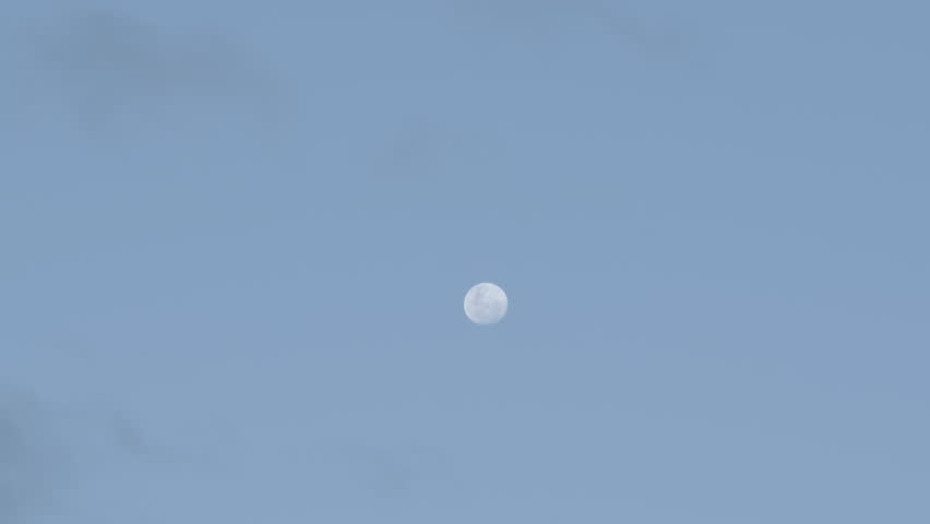 Time lapse of the blue sky with the Moon rising during day and clouds rolling past it