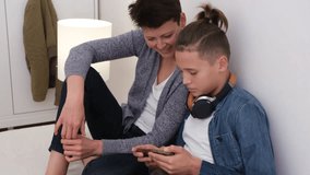Teenager boy addicted to technology watching social video at home with his mother. Child and mother communicate and play with the technological device mobile phone.