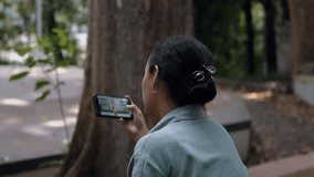 an Asian woman is watching a dancing video on her smartphone very seriously in a park