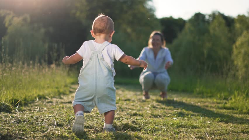 First steps. Childhood dream concept. Happy family in park on green grass. Mom teaches baby to take first steps. Happy mother day the first steps of cheerful kids in park on grass. First steps concept Royalty-Free Stock Footage #1106938345