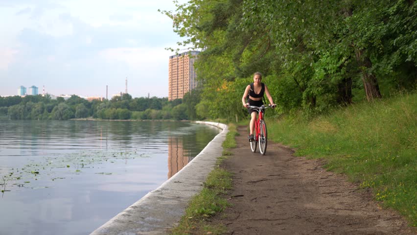 Young positive sports woman on a bicycle near the river in the city park