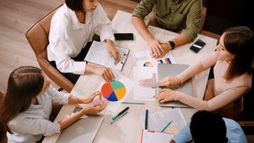 Employees report to manager about progress in work giving papers with diagrams. Multinational entrepreneurs sit at table in office holding meeting upper view slow motion - Powered by Shutterstock - Get 15% off with code: PIKWIZARD15