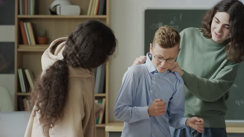 Panning medium shot of teen boys and girls spending break time in classroom teasing their nerd classmate | Shutterstock HD Video #1106949779