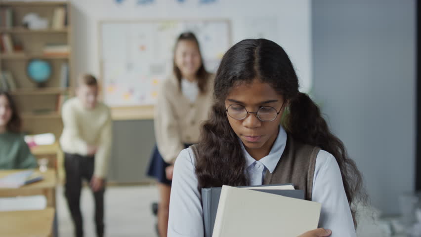 Selective focus shot of teen African American girl wearing eyeglasses holding books suffering bullying at school | Shutterstock HD Video #1106950459