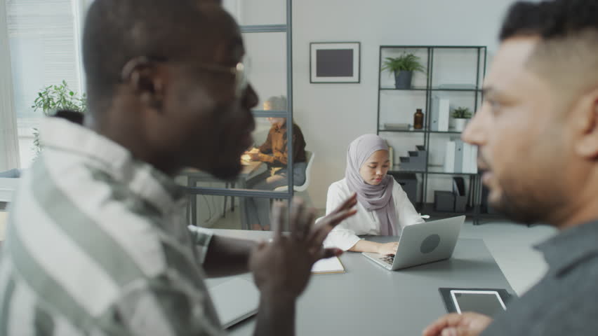 Selective focus shot of Muslim woman focusing on work while her male colleagues slandering her Royalty-Free Stock Footage #1106955353