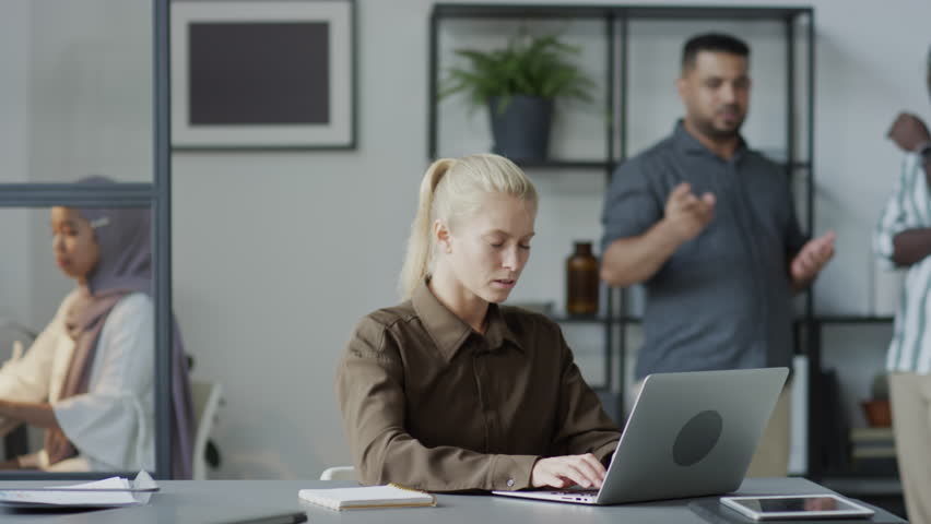 Selective focus shot of Caucasian female manager working on laptop trying to ignore annoying male co-workers slandering her Royalty-Free Stock Footage #1106955419
