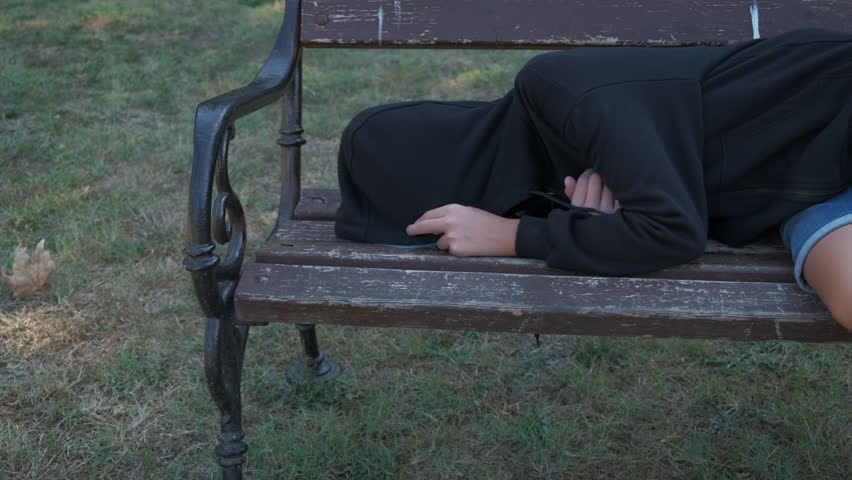 Homeless child. A lonely abandoned teenager lies on a park bench. Outcast teenager.